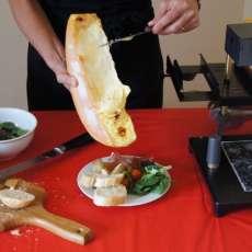 Raclette Cheese Is Being Scraped Off the Wheel Onto Plate