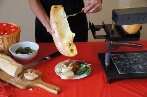 Raclette Cheese Is Being Scraped Off the Wheel Onto Plate